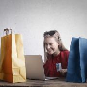 A woman shopping online surrounded by shopping bags. Credit: Canva